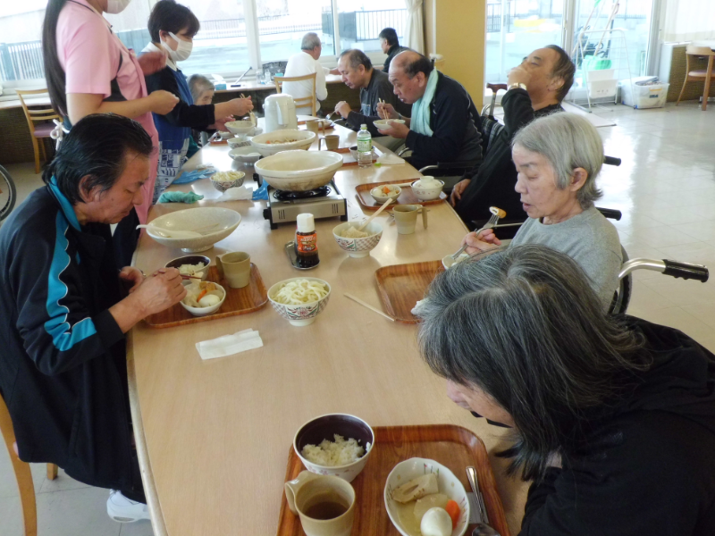 真ん中にカセットコンロがあるテーブルを複数人で囲んで食事をしています。