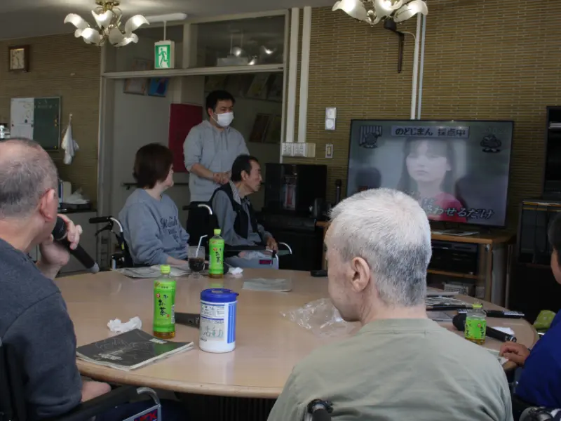 1人がマイクを持って歌っており、他の人はその人やテレビ画面を向いています