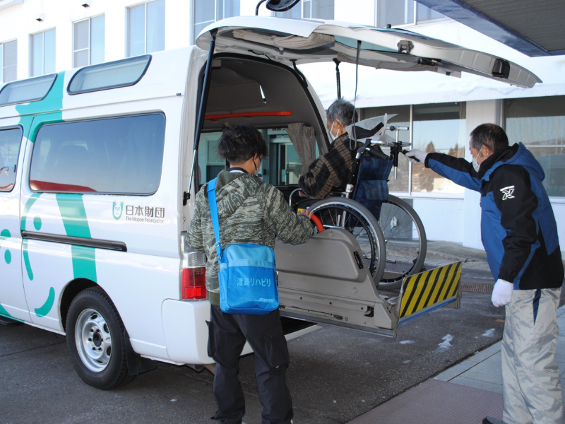 職員二人で、車椅子に乗った利用者の方を送迎車両にお乗せしているところです